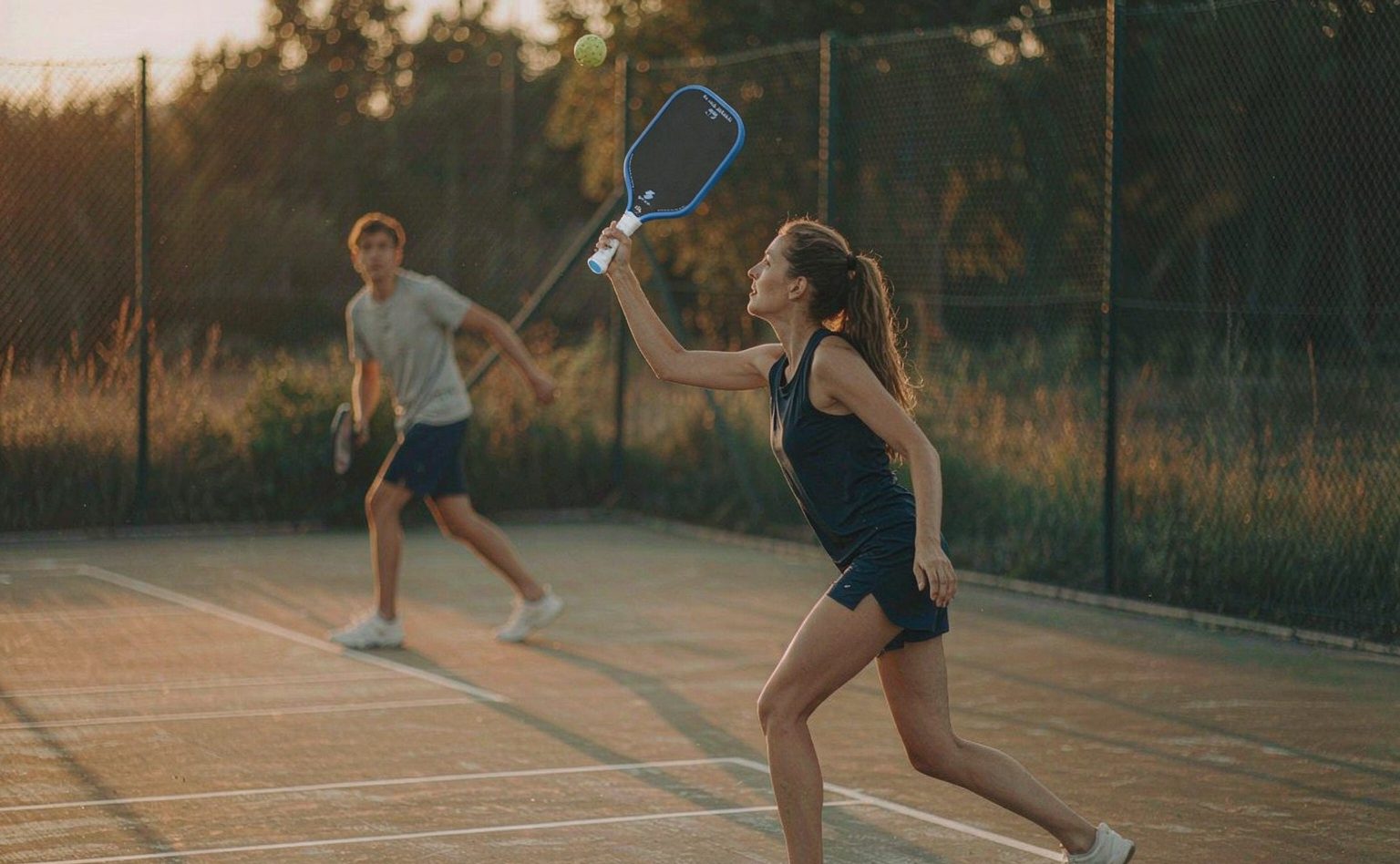 Two players rallying on an outdoor pickleball court at golden hour